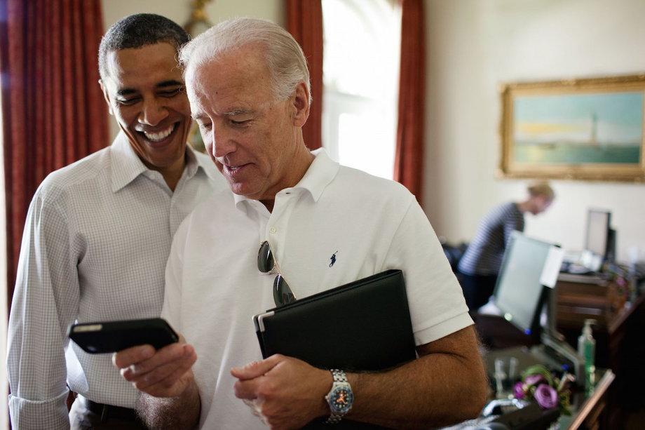 Biden and Obama look at an app on an iPhone in the Outer Oval Office.