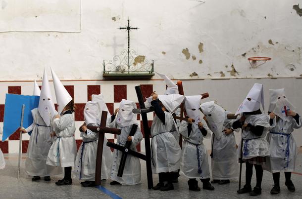 Children wearing hoods as penitents stand after taking part in a procession at a school on the eve o