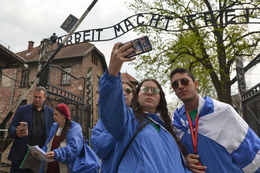 Ludzie robią sobie selfie przed tablicą "Arbeit Macht Frei" w pobliżu głównej bramy wjazdowej do Auschwitz