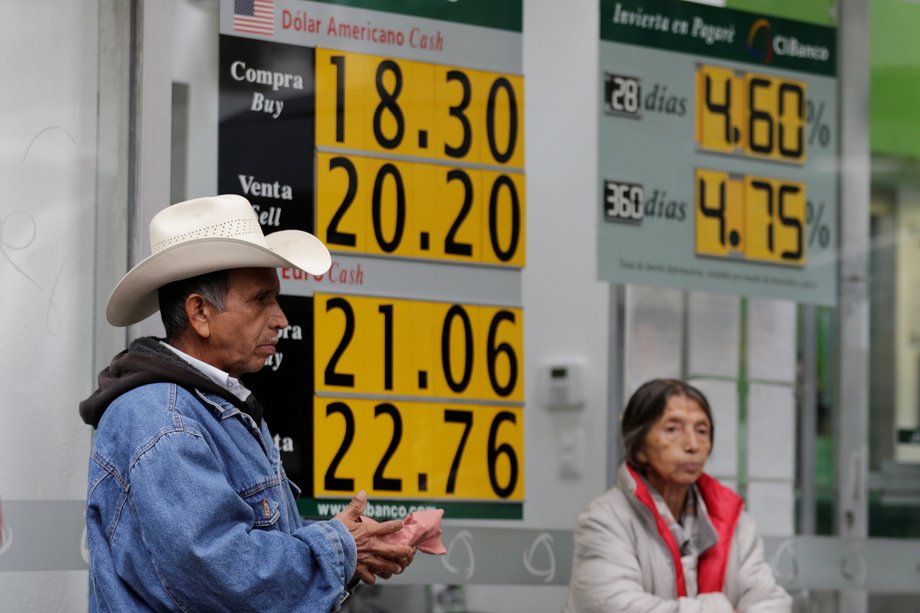 A couple stands in front of boards displaying the exchange rates of the Mexican peso against the US dollar, top, and the euro at a CI bank branch in Mexico City, Mexico, November 9, 2016.