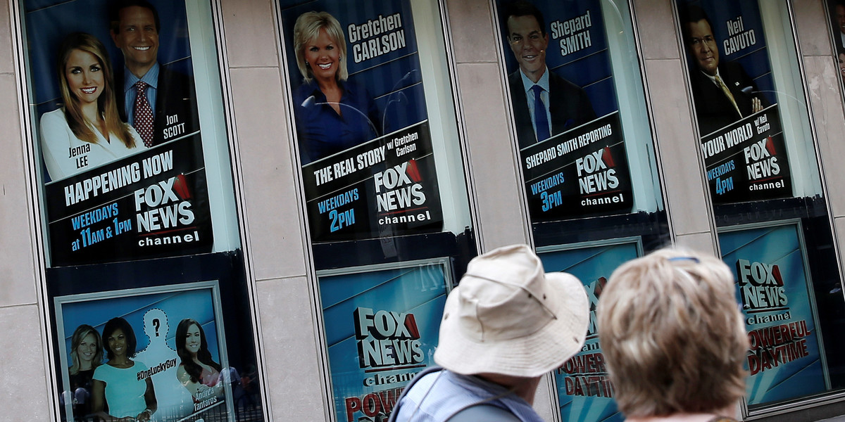 People walk by posters of Fox News personalities including Gretchen Carlson.