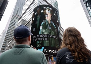 Posmatrači gledaju kako se na ekranu na Tajms skveru pojavljuje Ilon Mask, osnivač kompanije SpaceX, tokom inicijalne javne ponude akcija (IPO) kompanije u Nasdaq MarketSite centru, 12. juna 2026. godine u Njujorku.