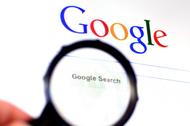 Hand holds Magnifying glass against Google homepage