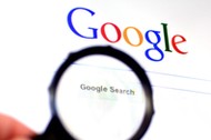 Hand holds Magnifying glass against Google homepage