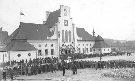 Uroczystości przed budynkiem dworca kolejowego w Gdyni w 1930 r. Po włączeniu w 1920 Gdyni do Polski i podjęciu decyzji o budowie miasta i portu, nastąpiło znaczne zwiększenie się ruchu pasażerskiego. W związku z tym w latach 1923-1926 powstał nowy, murowany i okazały gmach według projektu Romualda Millera, zbudowany w stylu narodowo-dworkowym