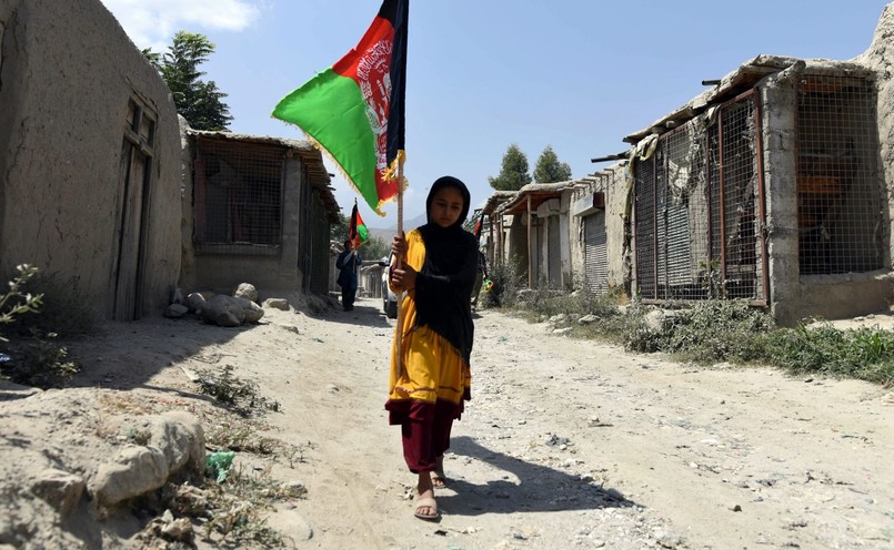 Aganistan. Kobieta niesie afgańską flagę wśród zabudowań odbitych z rąk bojowników z Państwa Islamskiego w prowincji Nangarhar