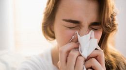 Woman blowing her nose on couch