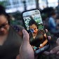 A Pokemon appears on the screen next to a woman as a man plays the augmented reality mobile game Pokemon Go by Nintendo in Bryant Park in New York City