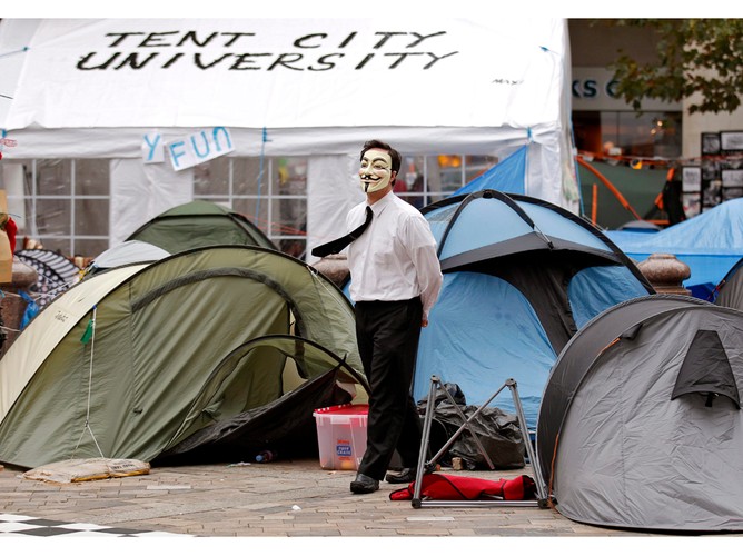 Ubrany w maskę uczestnik ruchu „Okupuj londyńską giełdę' w czasie porannego spaceru przez miasteczko namiotów w londyńskim City. 30 października 2011