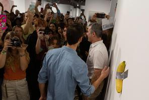 Art Basel visitors use their phones in front of a banana attached with duct-tape that replaces the artwork 'Comedian' by the artist Maurizio Cattelan, which was eaten by David Datuna, in Miami Beach