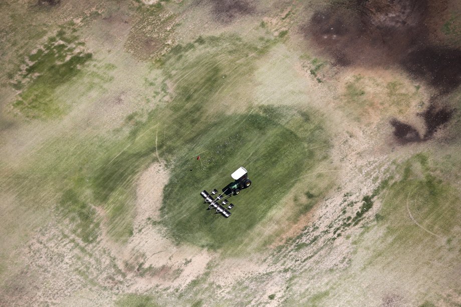 A tractor collects golf balls on a parched driving range in Palm Springs. According to state regulations introduced May 5, communities like Palm Springs — where residents use more than 165 gallons of water per person per day — would have to cut back their use by 35%.