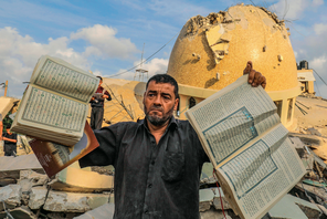 A man holds books of the Quran in front of a mosque destroyed by Israeli airstrikes.