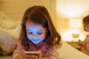 Little girl with smartphone lying in a bed, bedtime