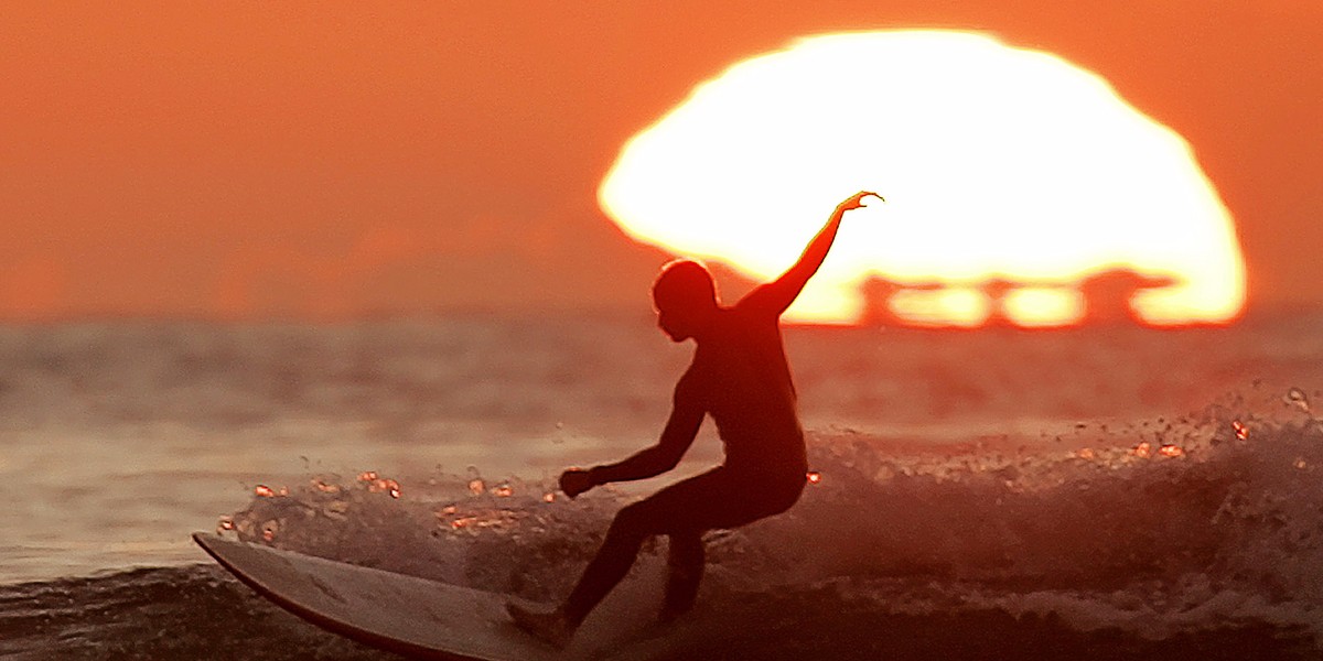 A surfer gets an early start on the Thanksgiving holiday as he rides a long board past the setting sun while surfing at sunset off Cardiff Beach in Cardiff, California, November 23, 2004.