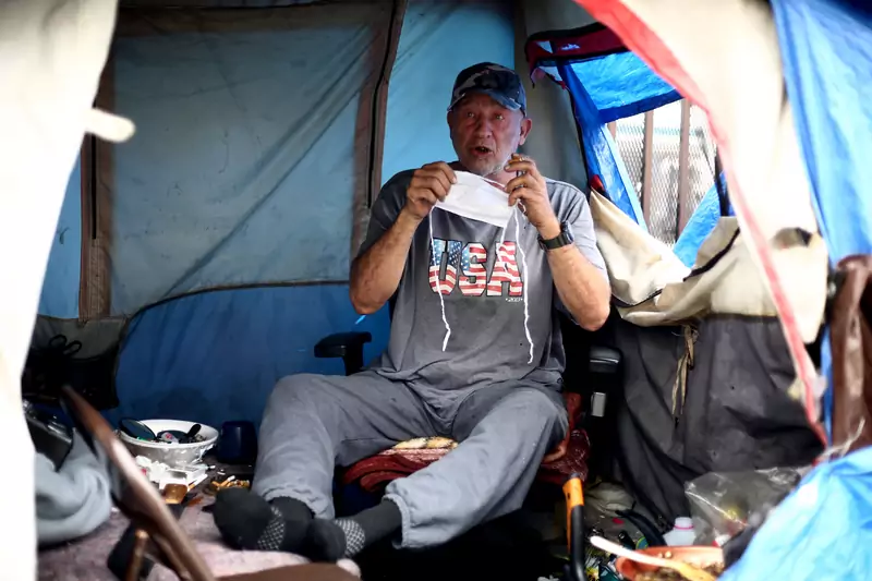 Bezdomny mieszkający w namiocie zakłada maskę ochronną, 20 kwietnia 2020
