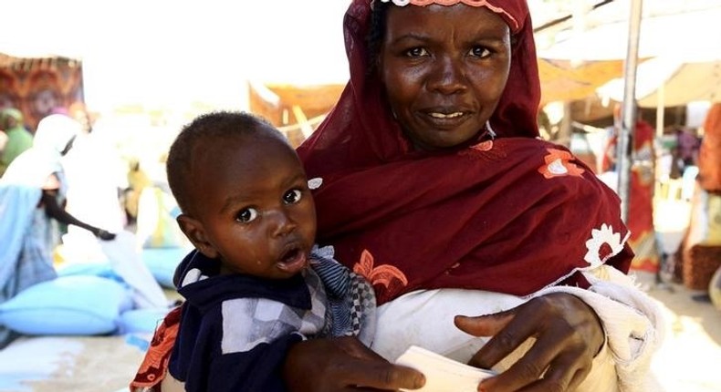 An internally displaced woman carries her child as she waits to receive food relief at a distribution center provided by the World Food Program at the Aboushouk camp in Al Fasher, North Darfur, Sudan, November 17, 2015. REUTERS/Mohamed Nureldin Abdallah