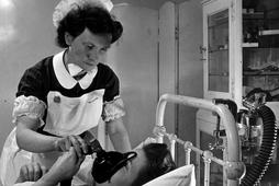 An expectant mother using an inhaler to take the pain killing drug trilene during labour, watched by a hospital midwife.