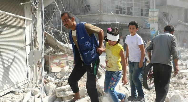 Syrians walk over rubble following air strikes on Aleppo on October 12, 2016