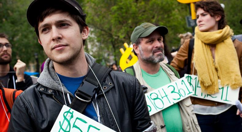 Protestors wearing signs with the amount of student debt they owe.
