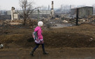 Girl walks near the debris of burnt buildings in the settlement of Shyra