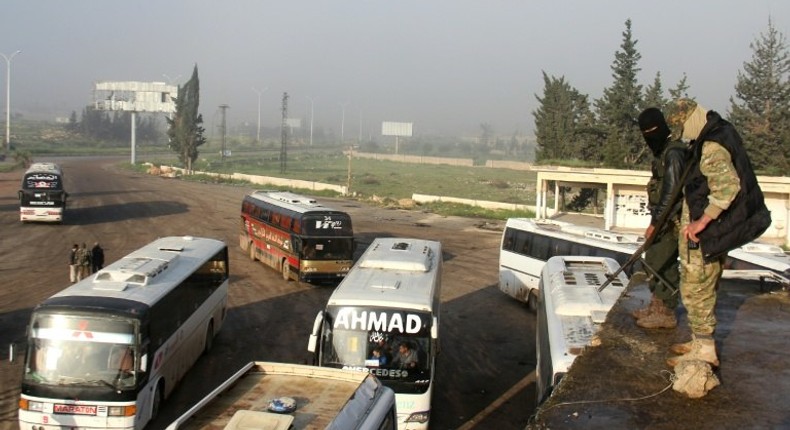 Syrian opposition fighters stand on top of a vehicle in rebel-held Rashidin, west of Aleppo city, as buses carrying people from government-held Fuaa and Kafraya arrive as part of an evacuation deal