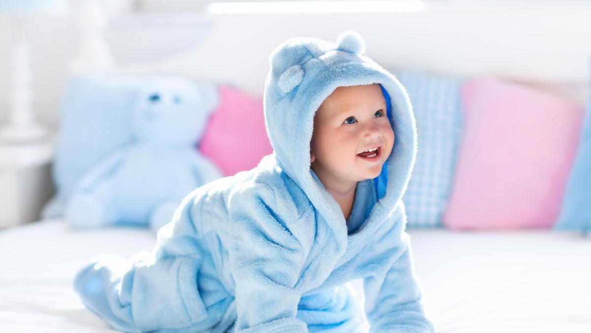 Baby in bathrobe or towel after bath on white bed