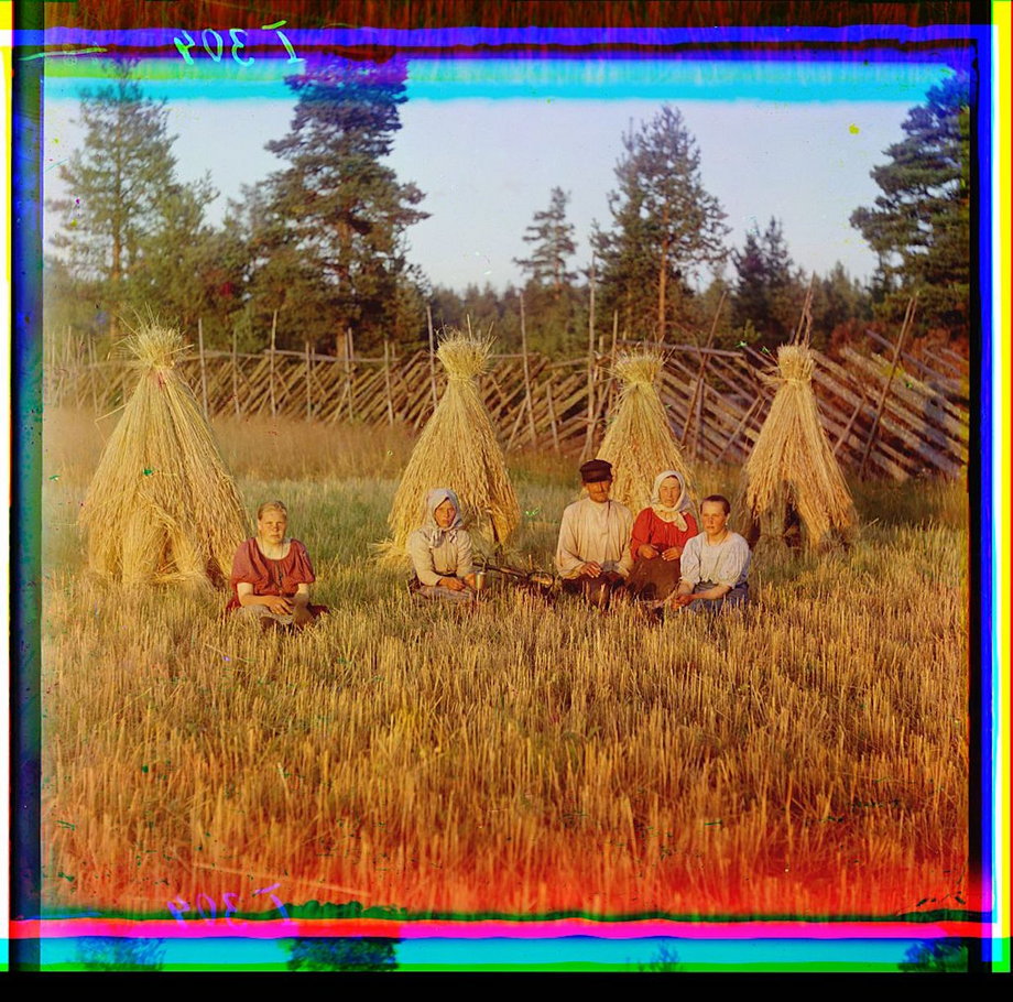 A family sits in front of hay stacks in a hay field during harvest time.