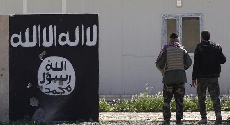 Shi'ite fighters stand near a wall painted with the black flag commonly used by Islamic State militants in the town of Tal Ksaiba, near the town of al-Alam March 7, 2015. REUTERS/Thaier Al-Sudani