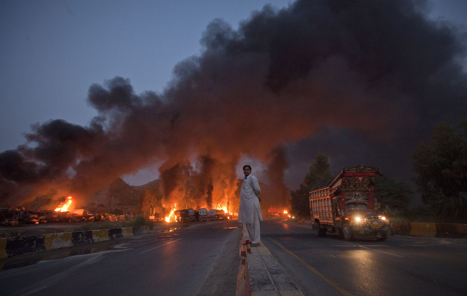 A local resident stands on the street median as he watches fuel tankers burn along the GT road in Nowshera, Pakistan