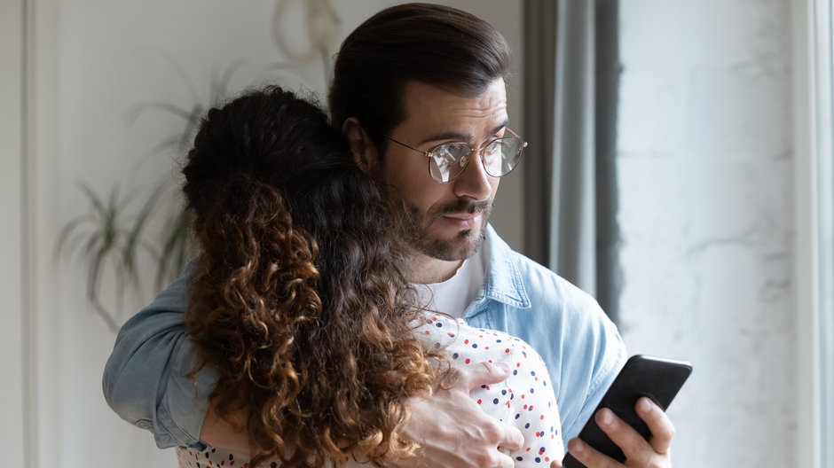 Mąż przytula żonę odpisując na wiadomości w telefonie