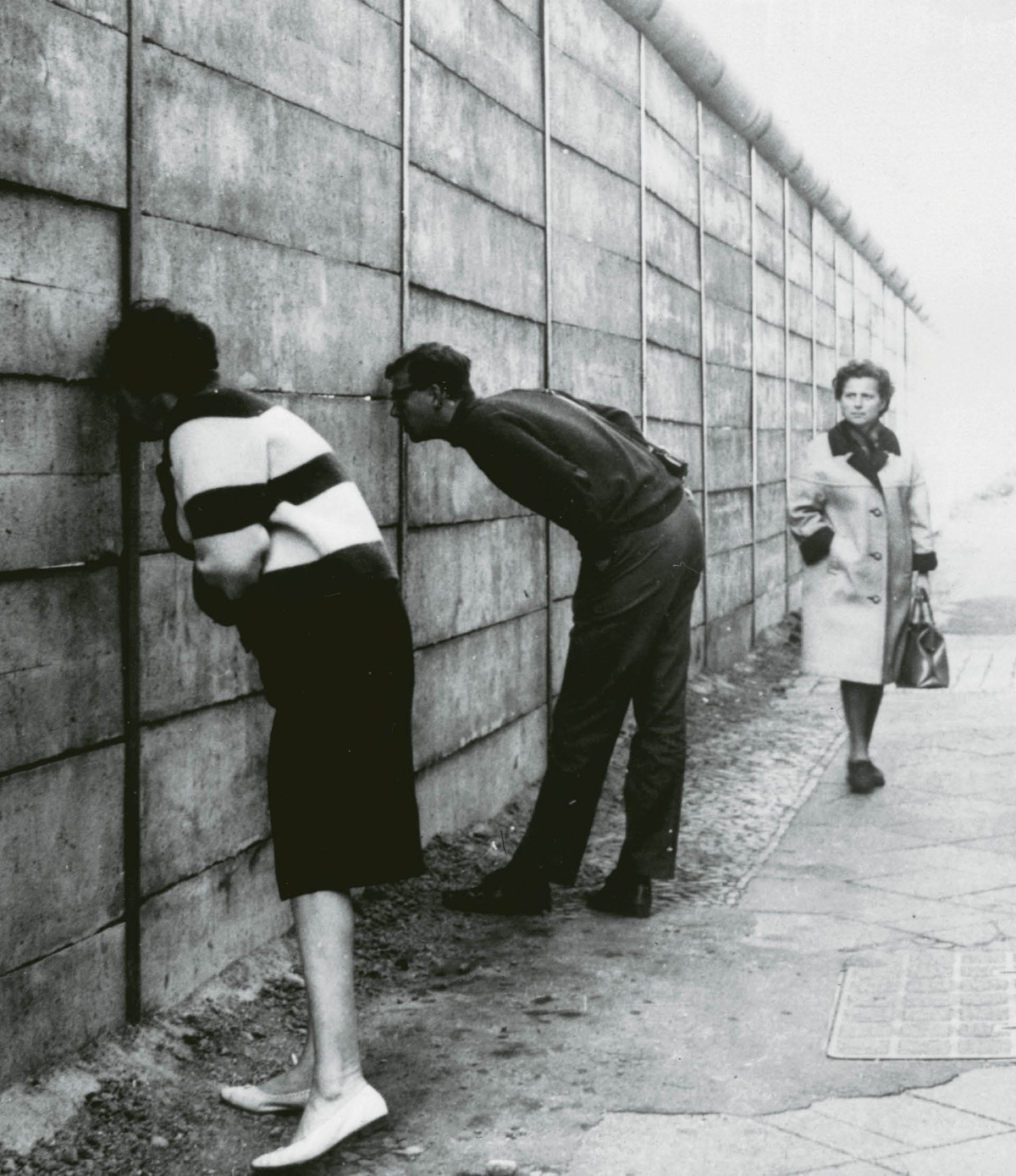 Mieszkańcy Berlina Zachodniego patrzą przez szpary w murze na wschodnią część miasta, 1966 r.