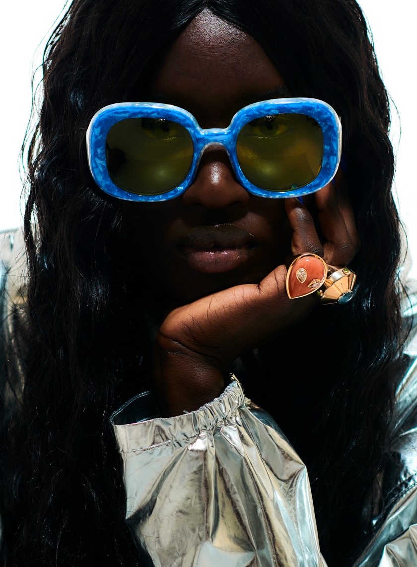 JULIAN ZIGERLI Windbreaker mit Kapuze zum Überziehen. ALINA ABEGG Ring Alien aus Gelbgold, mit Mondstein und Diamanten. Ring Micro Ufo aus Gelbgold, mit blauem Turmalin und Diamanten. Beide aus  der Cosmic-Escape-Kollektion. LARMA Sonnenbrille aus Azetat.