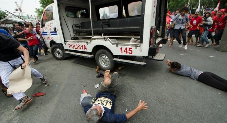 Protesters lie on the ground after being hit by a police van during a rally in front of the US embassy in Manila on October 19, 2016