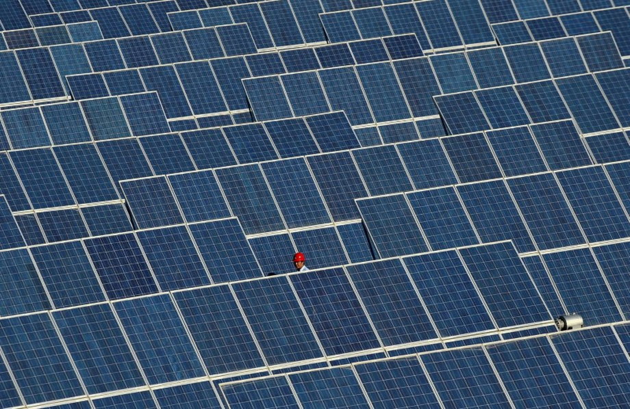 An employee walks between rows of solar panels at a solar power plant on the outskirts of Dunhuang