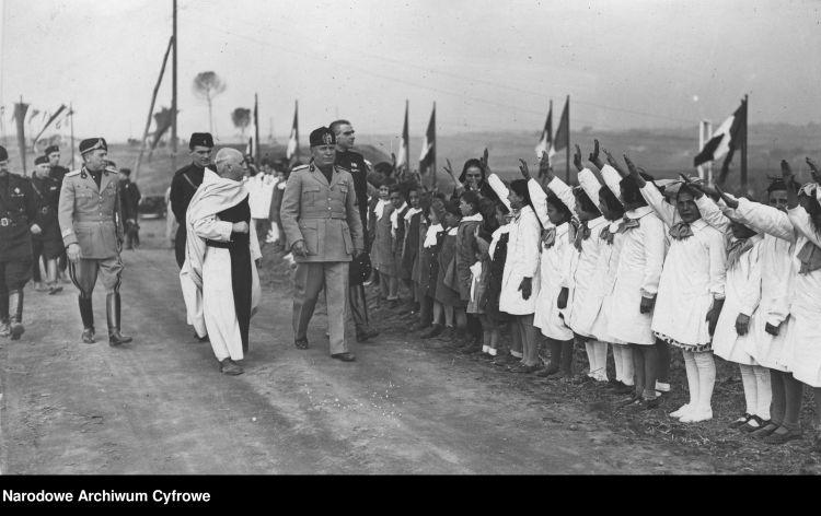 Benito Mussolini przechodzi przed szeregiem dzieci, które podrawiają go faszystowskim pozdrowieniem