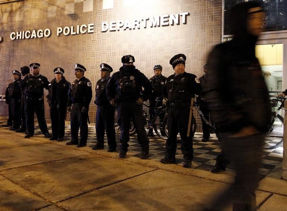 A protester walks past a line of police officers standing guard in front of the District 1 police headquarters in Chicago, Illinois November 24, 2015.