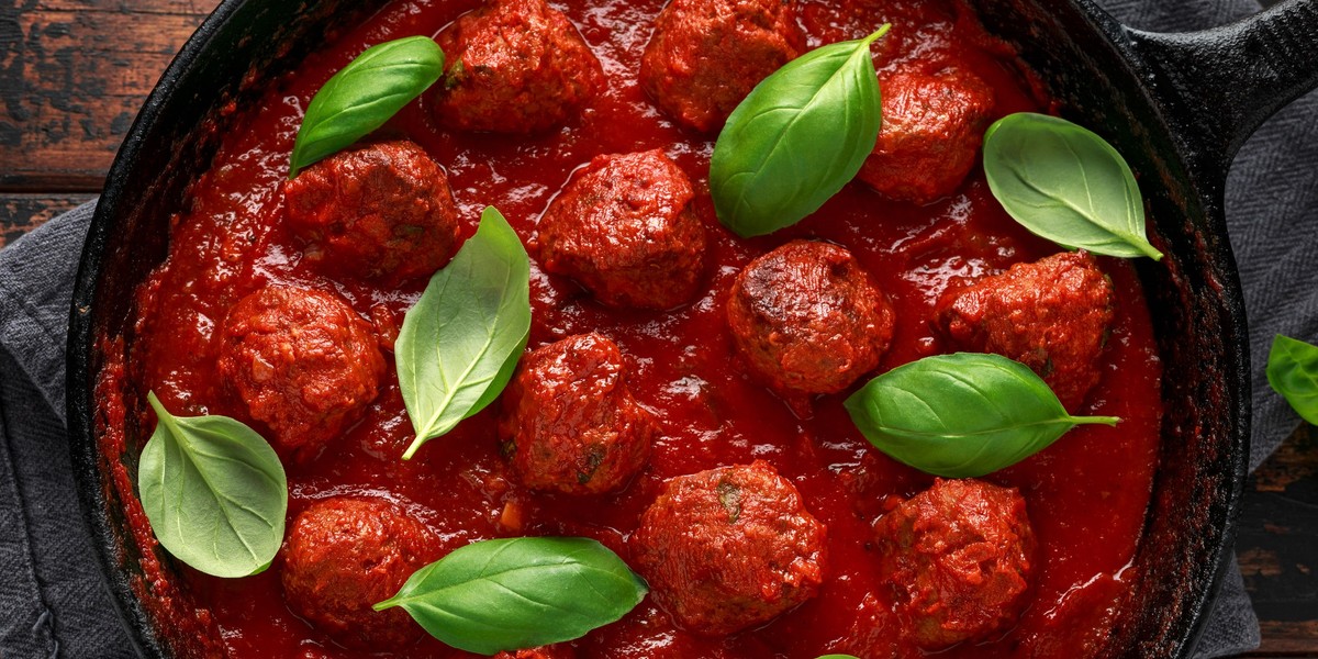 Homemade Meatballs in iron cast with sweet and hot tomato sauce, basil. On wooden table