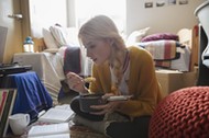 Female college student eating and studying on floor in dorm room