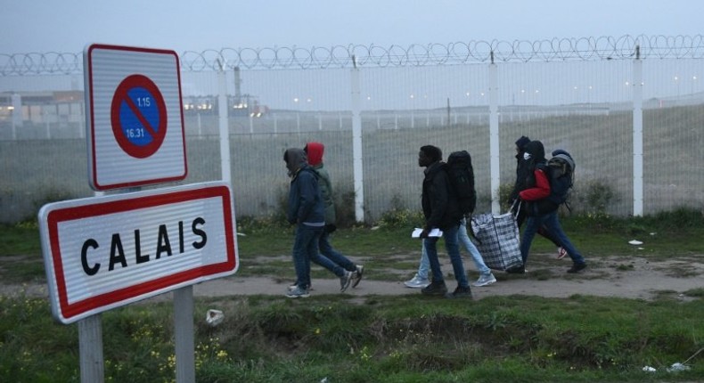 Migrants, carrying their luggage, walk past a Calais city limit sign as they head towards a meeting point set by French authorities as part of the full evacuation of the Calais Jungle camp, on October 24, 2016