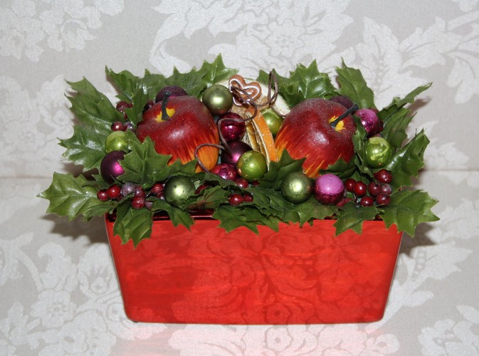 Świąteczny stroik w czerwonym naczyniu z jabłuszkami, bombkami i liśćmi ostrokrzewu. Autorka: Marta Jarosińska-Mańka