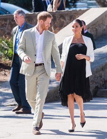 Meghan egy finom, pliszírozott fekete, térdig érő, ujjatlan ruhában lépett a nyilvánosság elé Marokkóban, amit egy fehér blézerrel és fekete nyitott hátú magas sarkúval viselt.