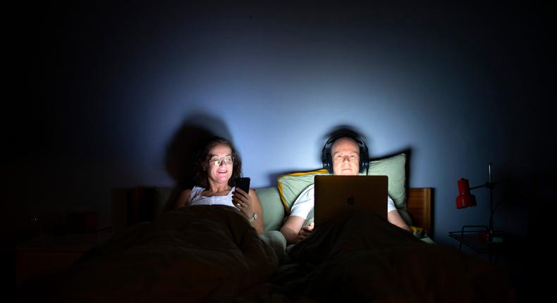 A woman looks at her phone, and a man watches his laptop in bed at night.Ute Grabowsky/Contributor/Photothek via Getty Images