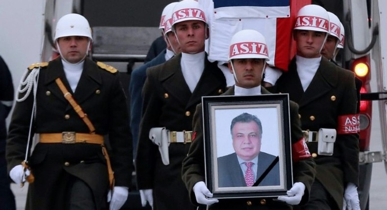 Members of a Turkish forces honour guard carry the Russian flag-draped coffin of late Russian Ambassador to Turkey Andrei Karlov and a picture of him during a ceremonial farewell with full state honours on the tarmac of Ankara's Esenboga Airport