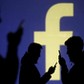 FILE PHOTO: Silhouettes of mobile users are seen next to a screen projection of Facebook logo in thi