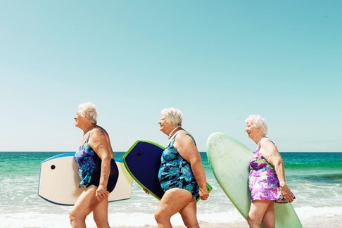 Three mature women on beach with surfboards