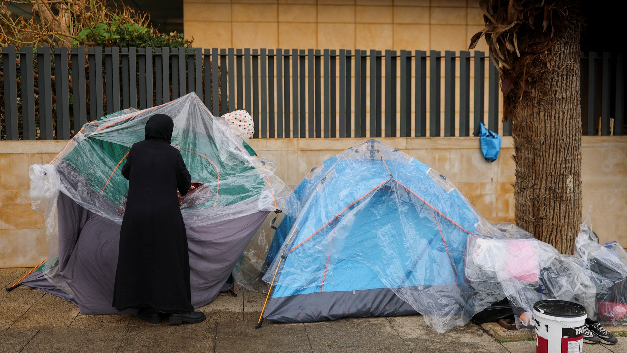 Žena zakrýva stan pred dažďom uprostred americko-izraelského konfliktu s Iránom.