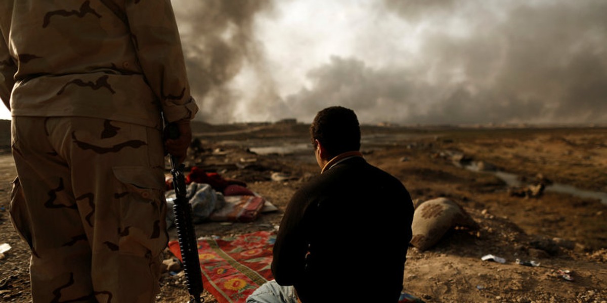 An Iraqi soldier stands next to a detained man accused of being an Islamic State fighter, at a check point in Qayyara, northern Iraq, October 30, 2016.