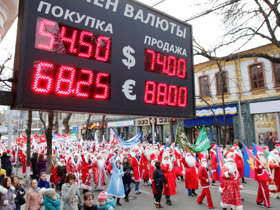 People dressed as Father Frost, the equivalent of Santa Claus, walk past a board showing currency exchange rates, during a parade in the Russian southern city of Krasnodar December 20, 2014.