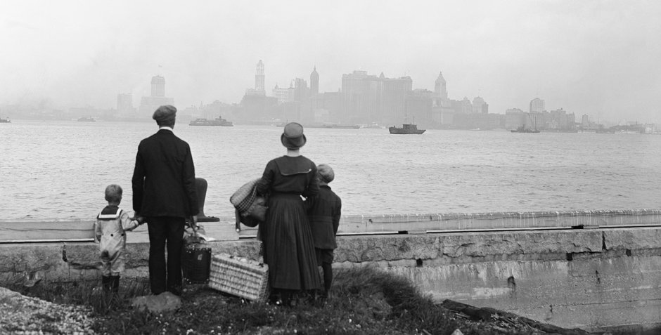 Rodzina imigrantów oczekująca na prom na Ellis Island, patrząca na panoramę Manhattanu w 1925 r.