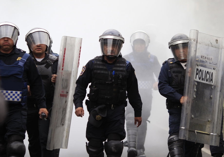 Riot police walk through a cloud of smoke from a fire extinguisher during a protest over the 43 missing Ayotzinapa students, near the Benito Juarez International airport in Mexico City, November 20, 2014.